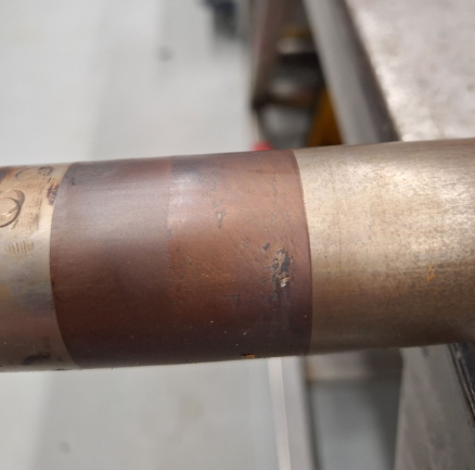 Metal shaft surface showing localized wear, discoloration, and scoring marks indicating mechanical degradation